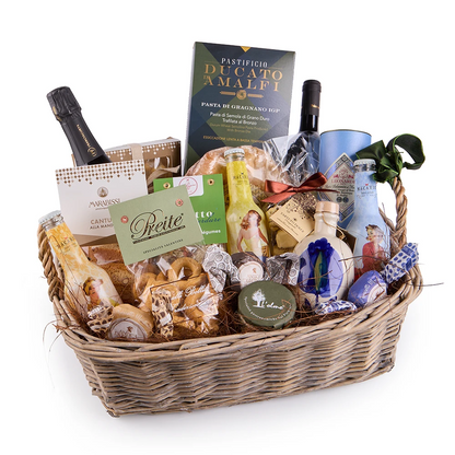 Italienischer Feinkost Geschenkkorb mit Pasta, Olivenöl, Wein, Süßwaren und mediterranen Delikatessen in einem geflochtenen Korb auf rustikalem Holztisch
